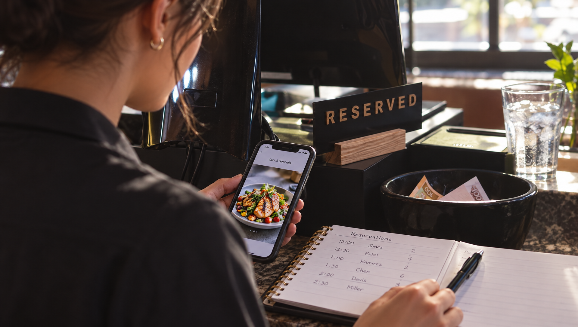 Une serveuse consulte son téléphone à côté du cahier de réservations.
