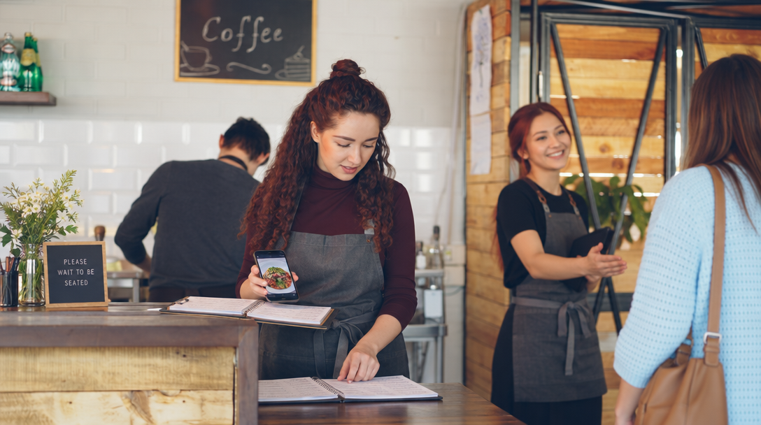 Une gérante compare son téléphone et son carnet de réservations au comptoir.