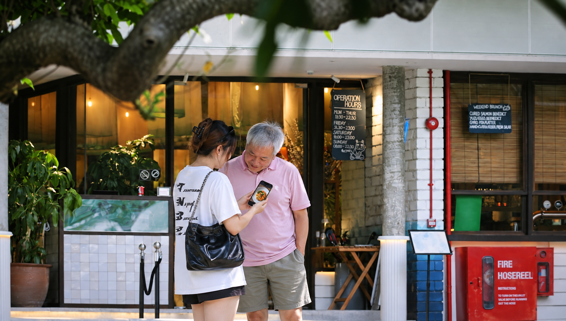 Deux amis consultent un téléphone devant l’entrée d’un restaurant.