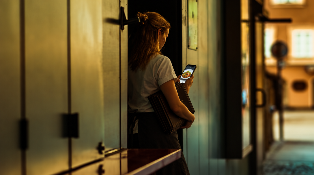 A restaurant manager holds a phone showing a dish in a hallway.